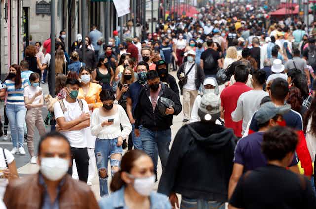 A crowded city street with lots of people walking close together and wearing masks