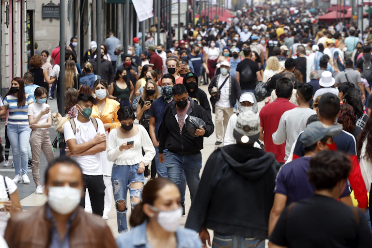 A crowded city street with lots of people walking close together and wearing masks