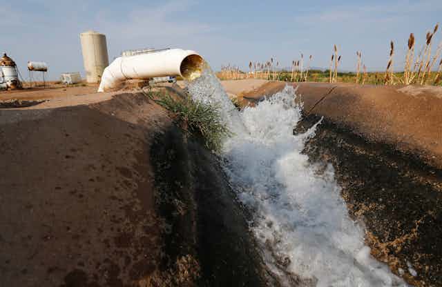 A large pipe discharges water into a dirt-lined canal