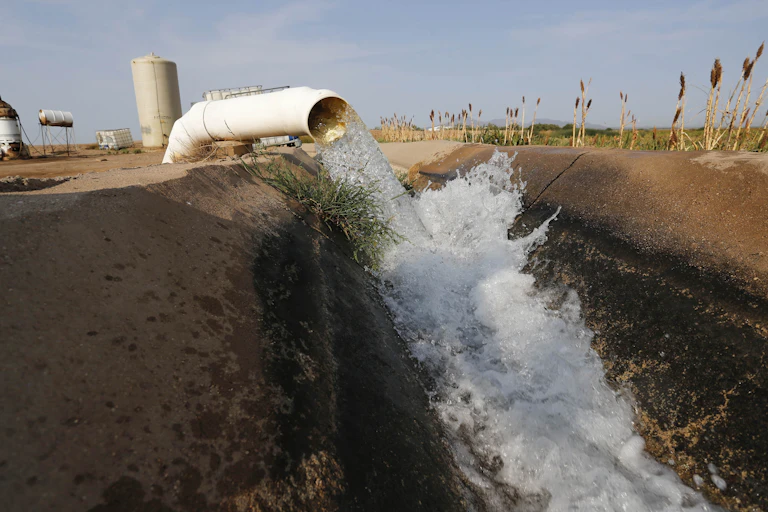A large pipe discharges water into a dirt-lined canal