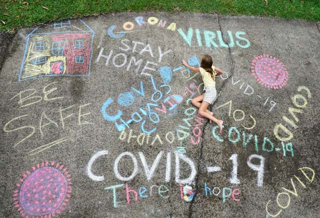 Girl drawing chalk message, 'be safe','there is hope', 'Corona'