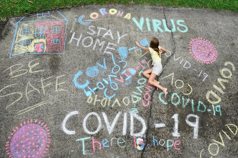 Girl drawing chalk message, 'be safe','there is hope', 'Corona'