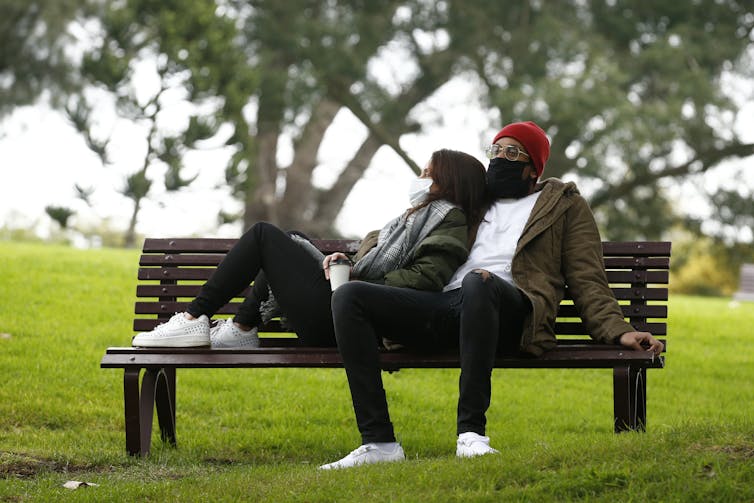 Couple in masks, flopped on a park bench.