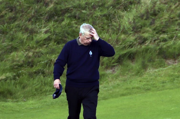 Prince Andrew on a golf course with his hand on his head.