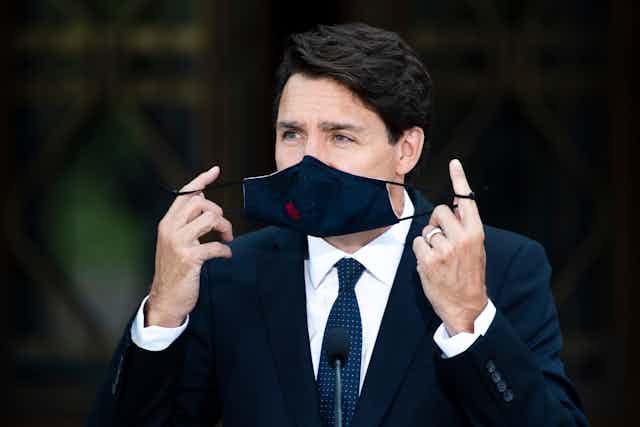Prime Minister Justin Trudeau's fingers are wrapped around his facemask that still covers part of his face.