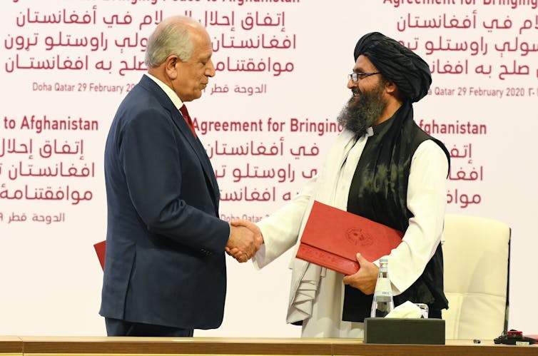 Khalilzad and Taliban co-founder shake hands.
