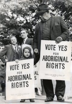 Old black and white photo. A man and a child hold signs reading 'vote yes for Aboriginal rights.'