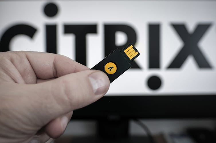 Hand holds up a YubiKey USB with the text 'Citrix' in the background.