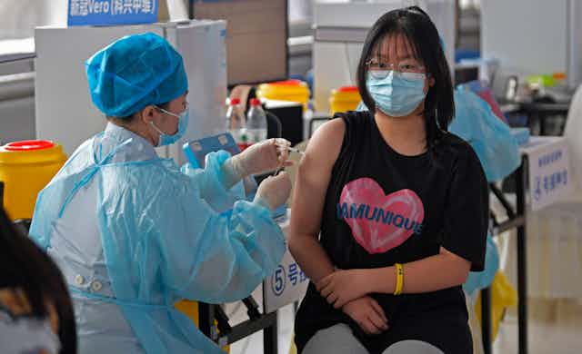 A nurse in PPE vaccinated a young woman in a mask.