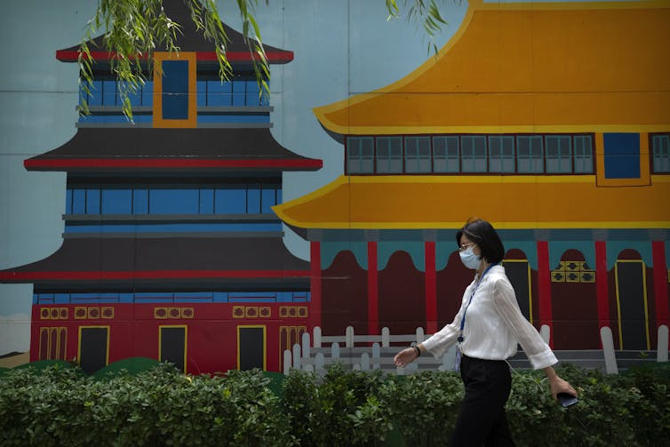 Woman in a mask talks past a colourful temple.