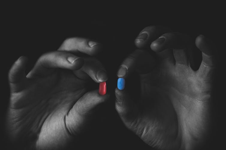 Two hands holding up a red and a blue bill. Other than the pills, the image is in black and white.