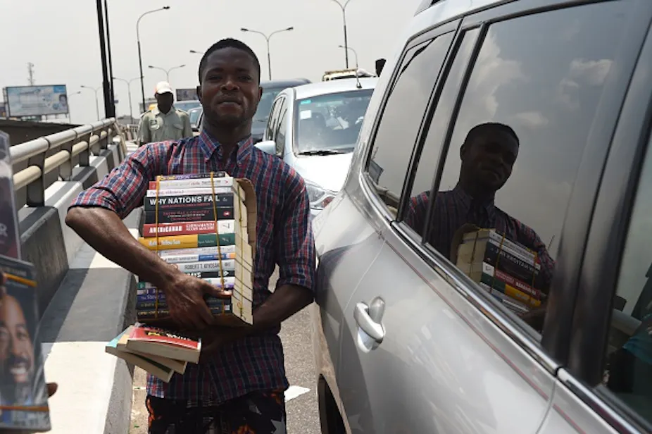 Jovem carregando uma pilha de livros ao lado de um carro na estrada