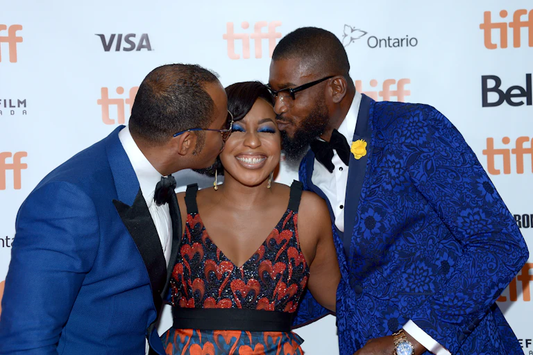 Two men kissing a woman on the cheeks.