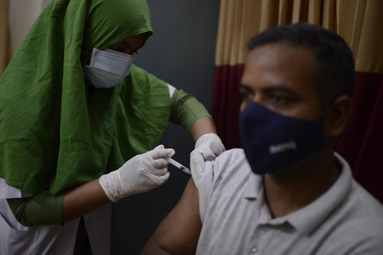 A man wearing a mask receives a shot of vaccine from a woman wearing a green head scarf in Dhaka, Bangladesh