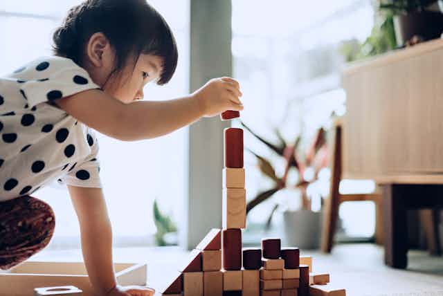 A toddler stacks building blocks on a floor