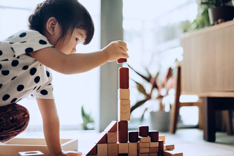 A toddler stacks building blocks on a floor