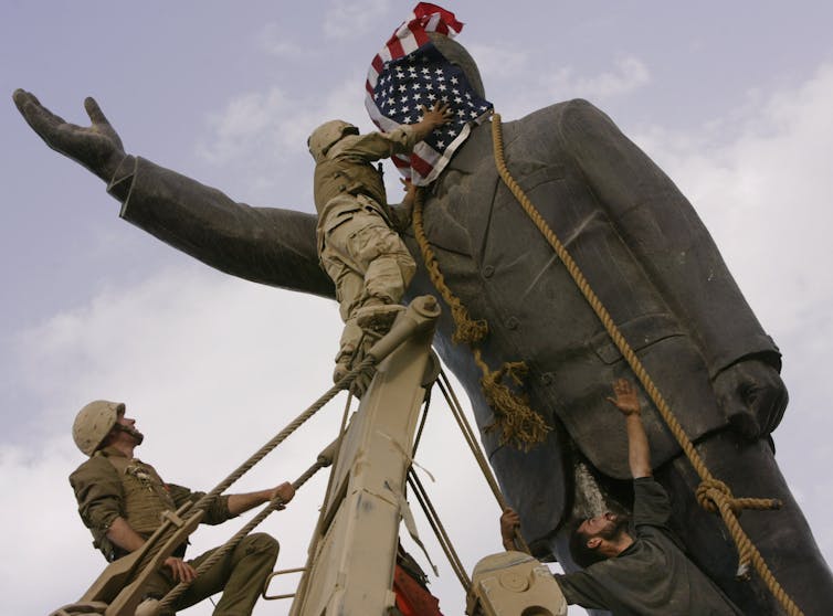 A man on a ladder covers a statue's face with a U.S. flag