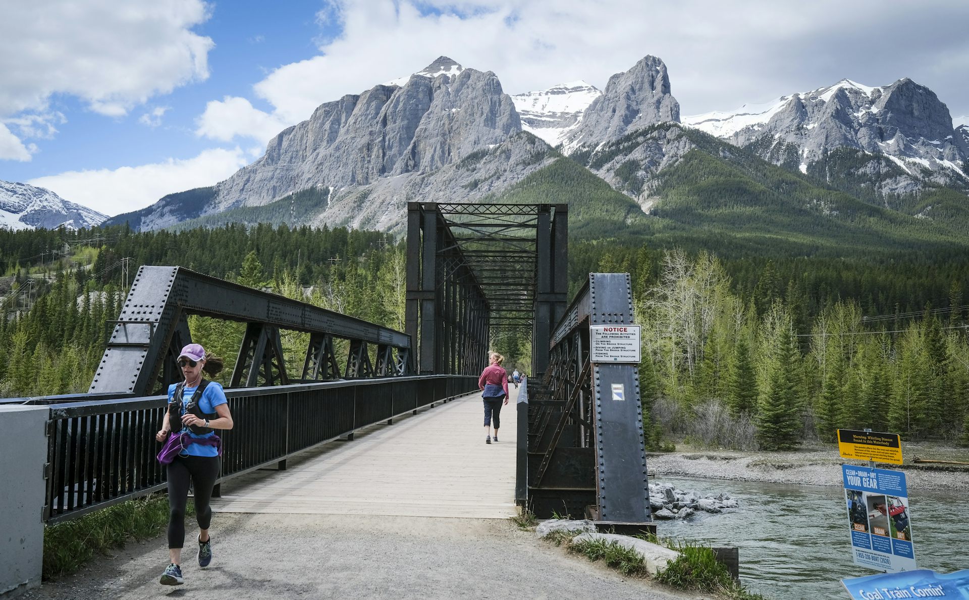 A woman runs on an old railway bridge with mountains in the background.