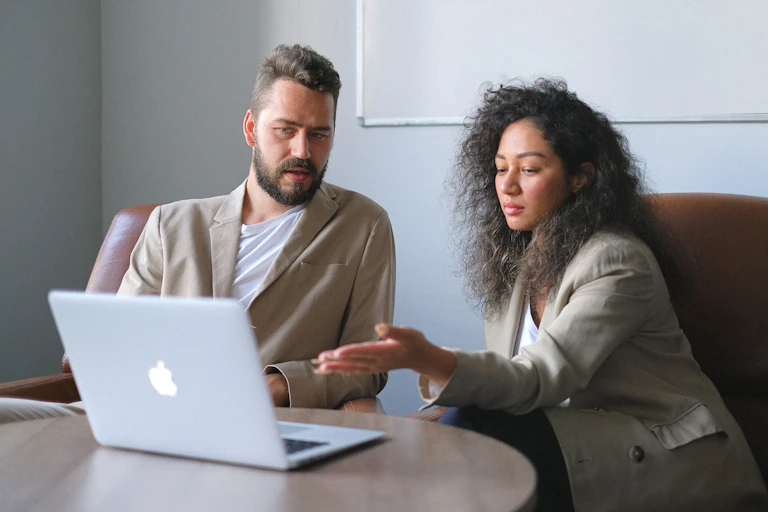 Female supervisor gives feedback to man as they look at laptop screen while seated at table