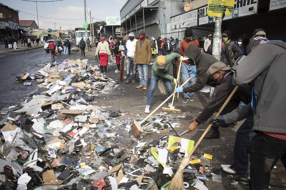  Men and women use brooms to sweep away debris on a street.