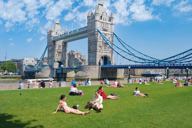 People sit on grass bank near Tower Bridge.
