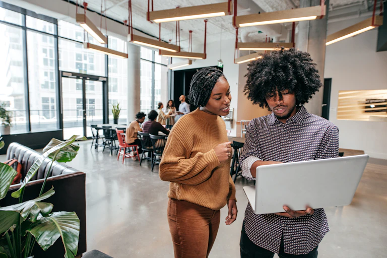 Young woman and young man in a modern commercial interior space, looking at a laptop computer