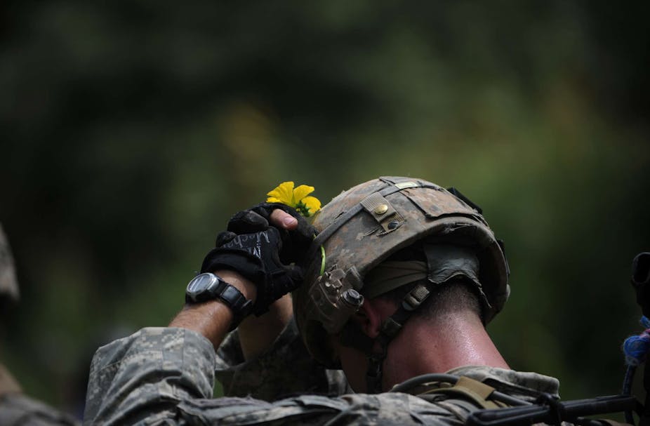 A US soldier in Afghanistan attaches a yellow flower to his helmet.
