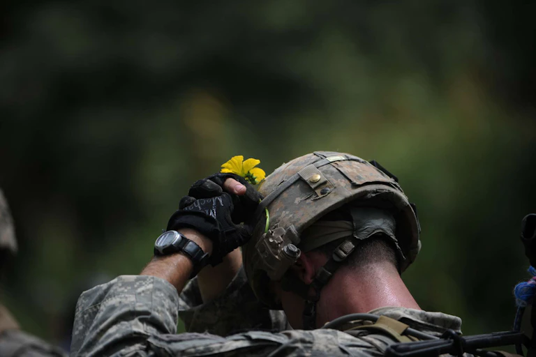 A US soldier in Afghanistan attaches a yellow flower to his helmet.
