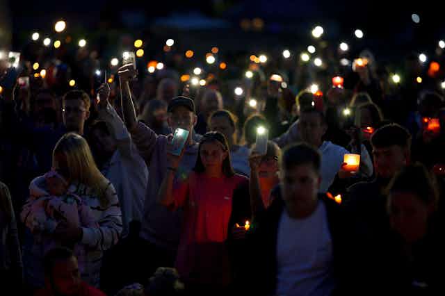 Attendees holding candles and phone flashlights at a vigil. 