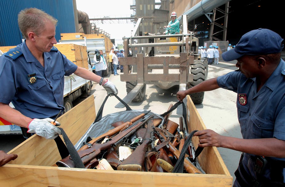 Two police officers load a bag full of rifles onto a forklift to be burnt in a furnance.