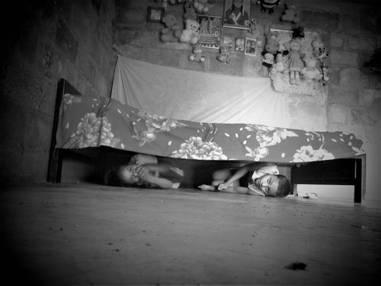 Two children conceal themselves under a bed.