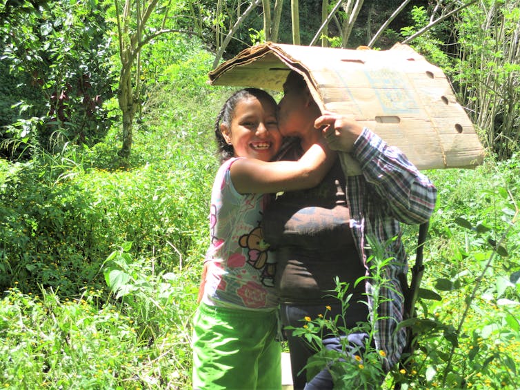 A person holding cardboard overhead hugs a smiling child.