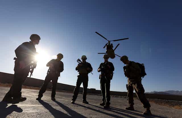 Soldiers stand silhouetted by the sun as a helicopter flies overhead