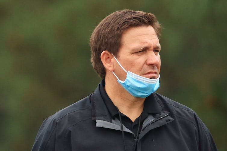 Florida Gov. Ron DeSantis in a black jacket with a mask pushed below his mouth.