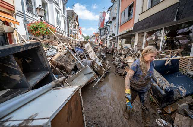 A woman walks through muddy streets lined with debris in a German village
