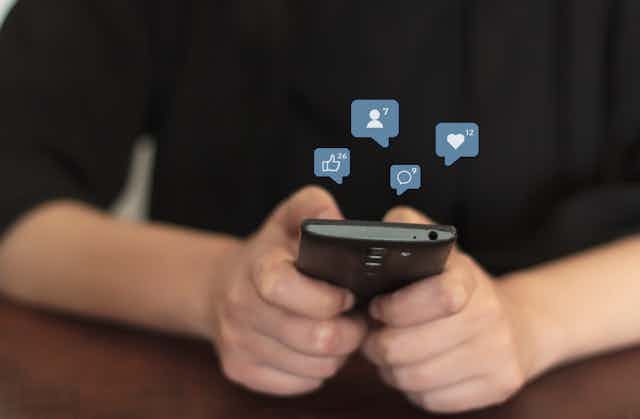 Image of a woman's hands typing on a smartphone with social media icons floating above them.