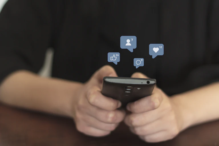 Image of a woman's hands typing on a smartphone with social media icons floating above them.