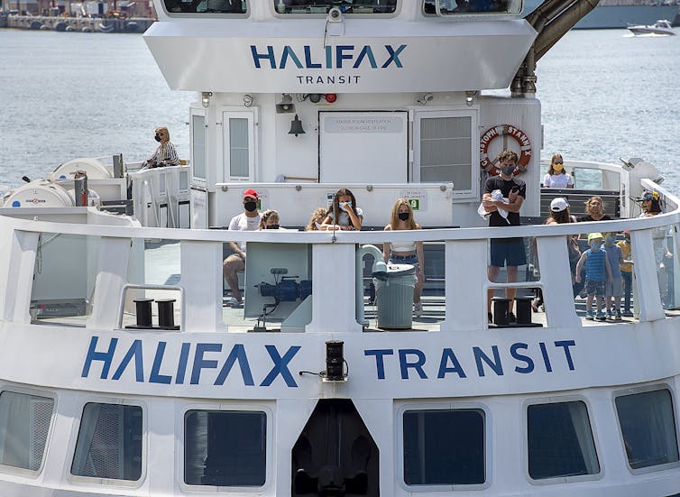 Passengers wear face masks on a Halifax Transit ferry.  The ferry is seen with a dozen passengers on the upper deck, with the Port of Halifax peaking in the background.