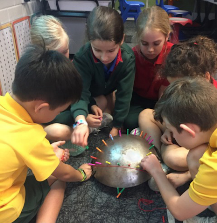Primary school children moving magnetic pins around a shiny metal domed surface