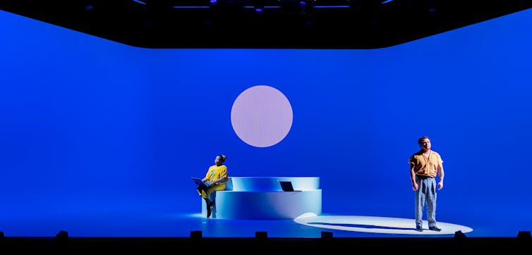 Production image: two people on a blue stage