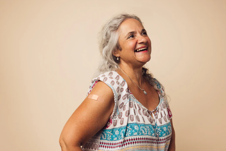 A smiling senior woman with a band-aid on her upper arm.