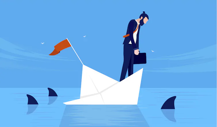 Businessman on sinking boat surrounded by sharks.