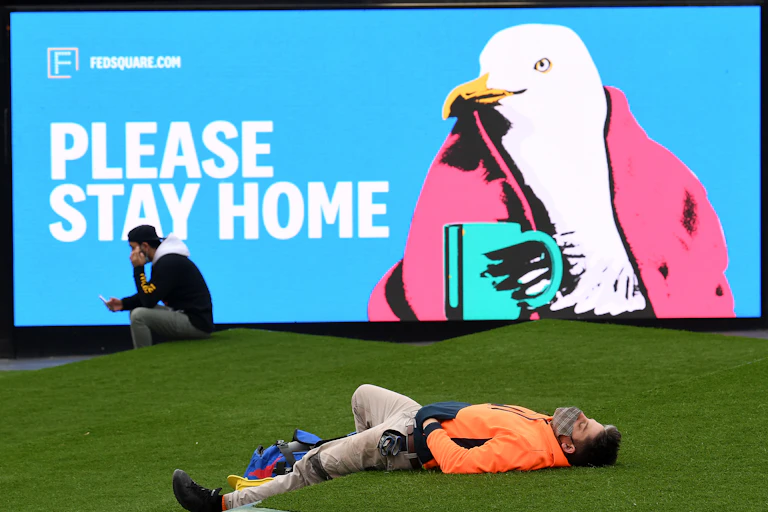 Masked Australian people outside standing in front of a sign saying: 'Please stay home'