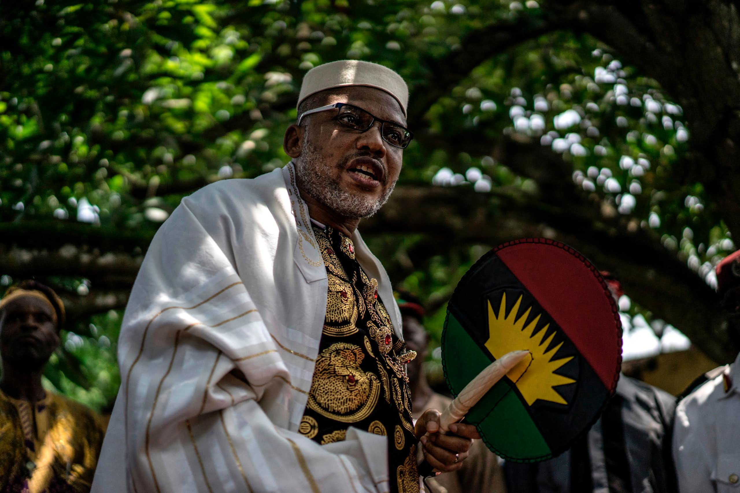 A man in traditional Igbo attire, standing under a tree.