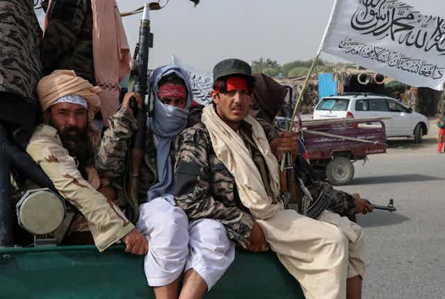 Taliban fighters holding guns and a flag on the back of a truck. 