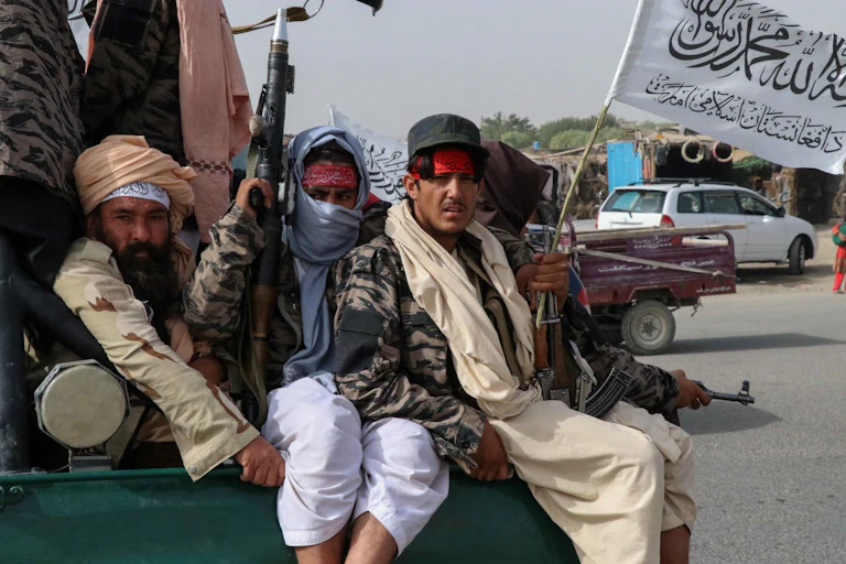 Taliban fighters holding guns and a flag on the back of a truck.