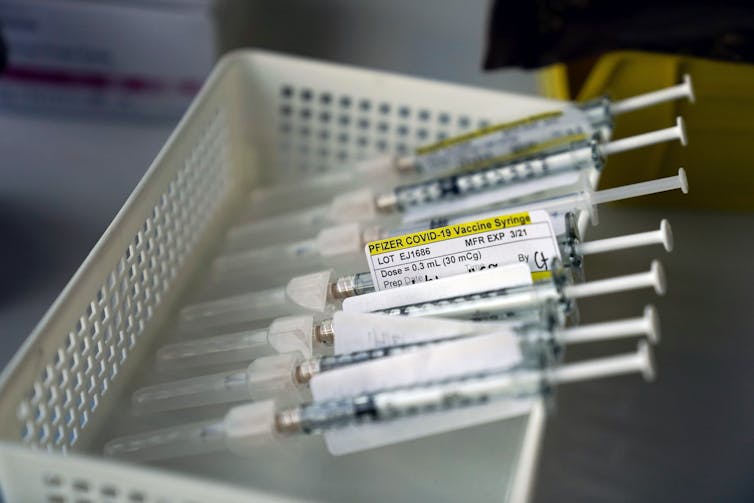 Several syringes containing diluted 0.3 mL doses of Pfizer vaccine sit in a box