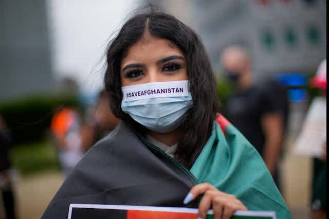 A woman wears a protective face mask reading #SAVEAFGANISTAN during a protest 