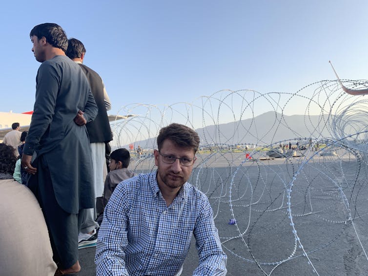 Hanif Sufizada sitting in front of barbed wire at the edge of an airport tarmac.