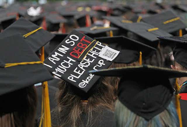 A college graduation cap reads, "I AM IN SO MUCH DEBT PLEASE HELP."